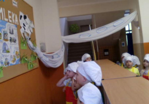 Dzieci w strojach kucharzy przy tablicy z wystawą "Rzeka mleka".